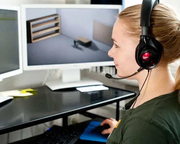 Studierende sitzt mit Headset vor zwei Bildschirmen