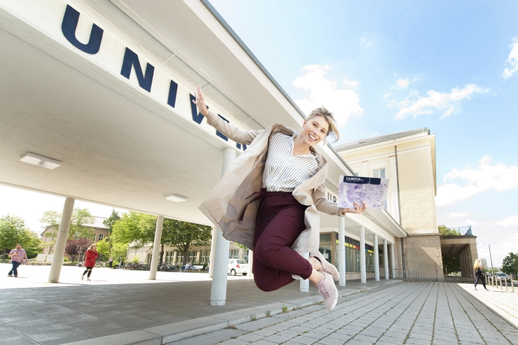 Hüpfende Studentin vor Haupteingang der Uni